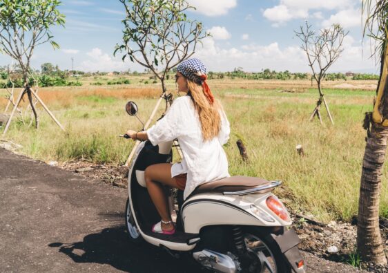 Trendy young woman riding motorcycle in rural area on sunny day