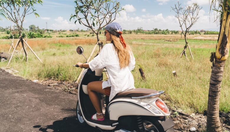 Trendy young woman riding motorcycle in rural area on sunny day