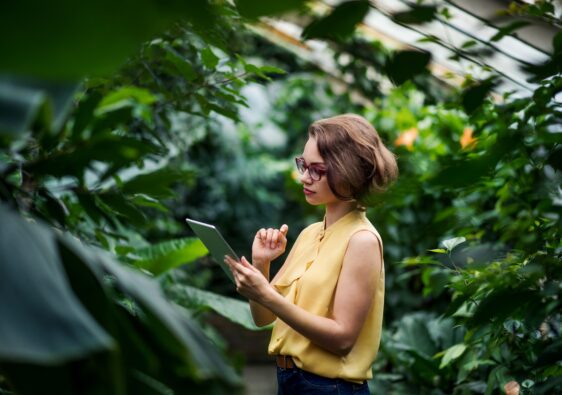 Young woman standing in greenhouse in botanical garden, using tablet