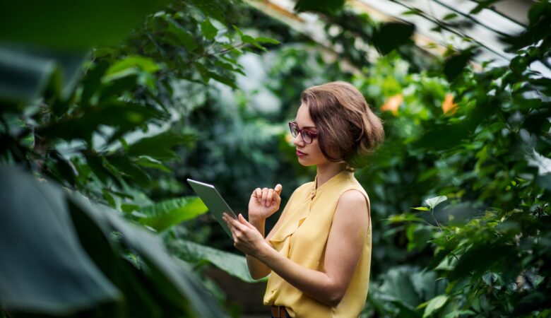 Young woman standing in greenhouse in botanical garden, using tablet